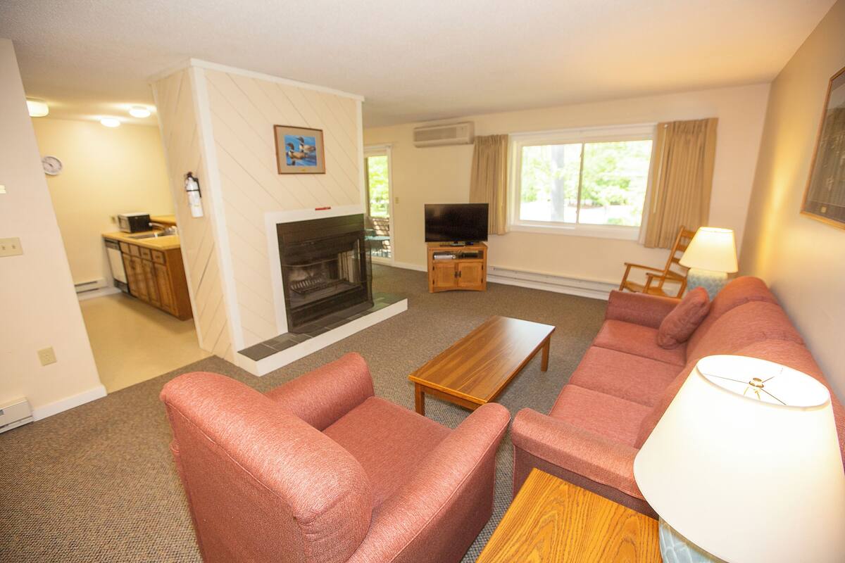 A living room with a fireplace, sofa, television, and a dining area with a table and chairs.