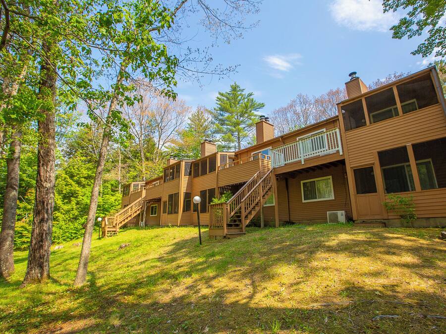 A two-story wooden cabin with a balcony, surrounded by trees.