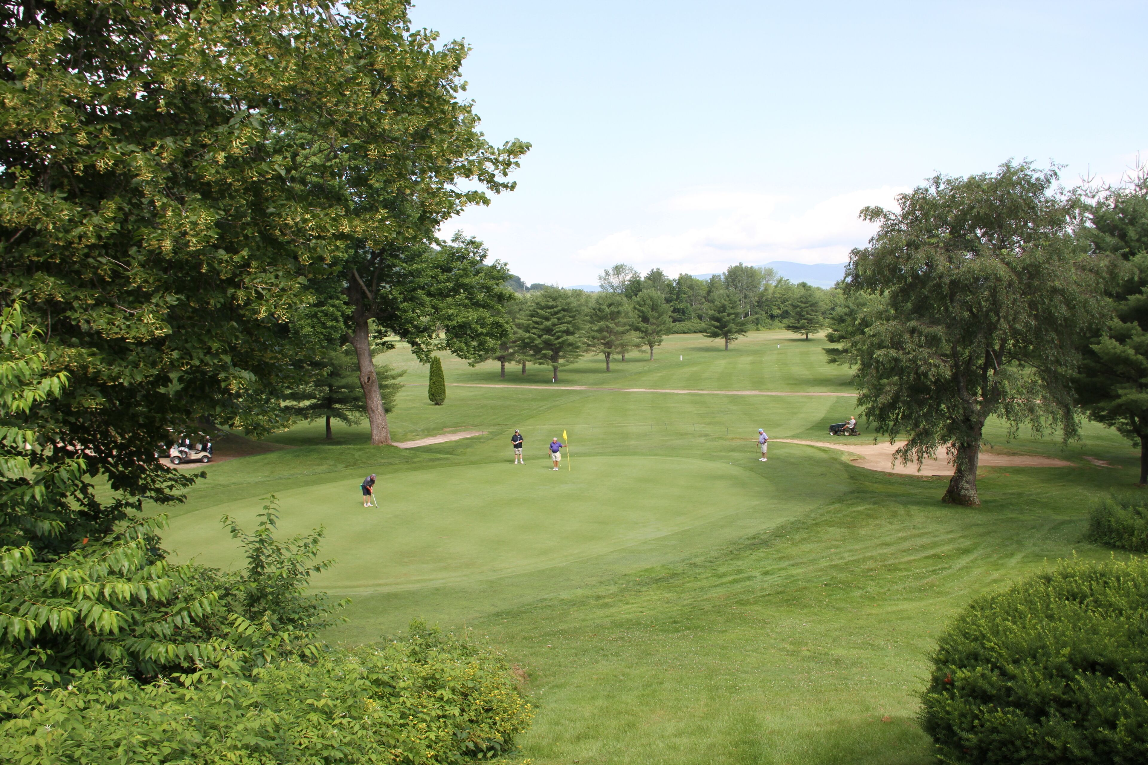 Un parcours de golf avec une pelouse bien entretenue, des arbres et un ciel dégagé.