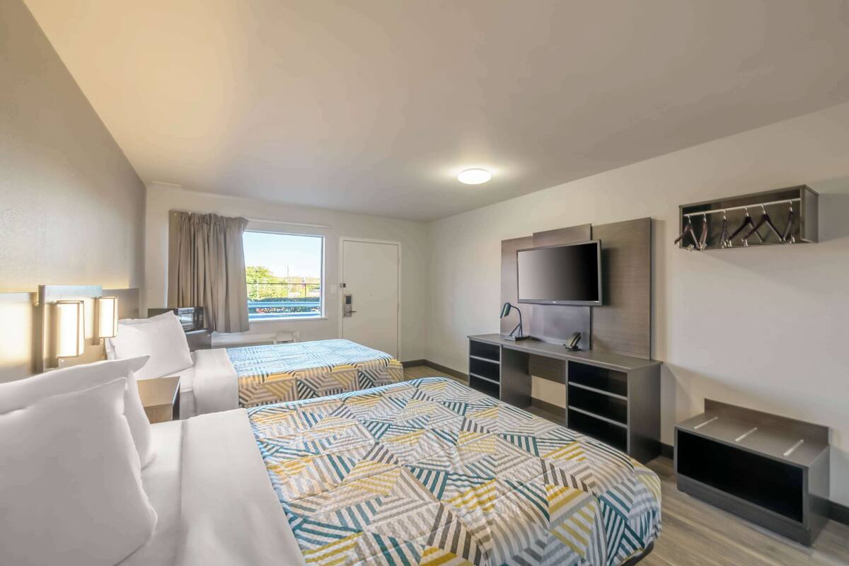 A hotel room with two beds, a TV, a desk, and a window with curtains.
