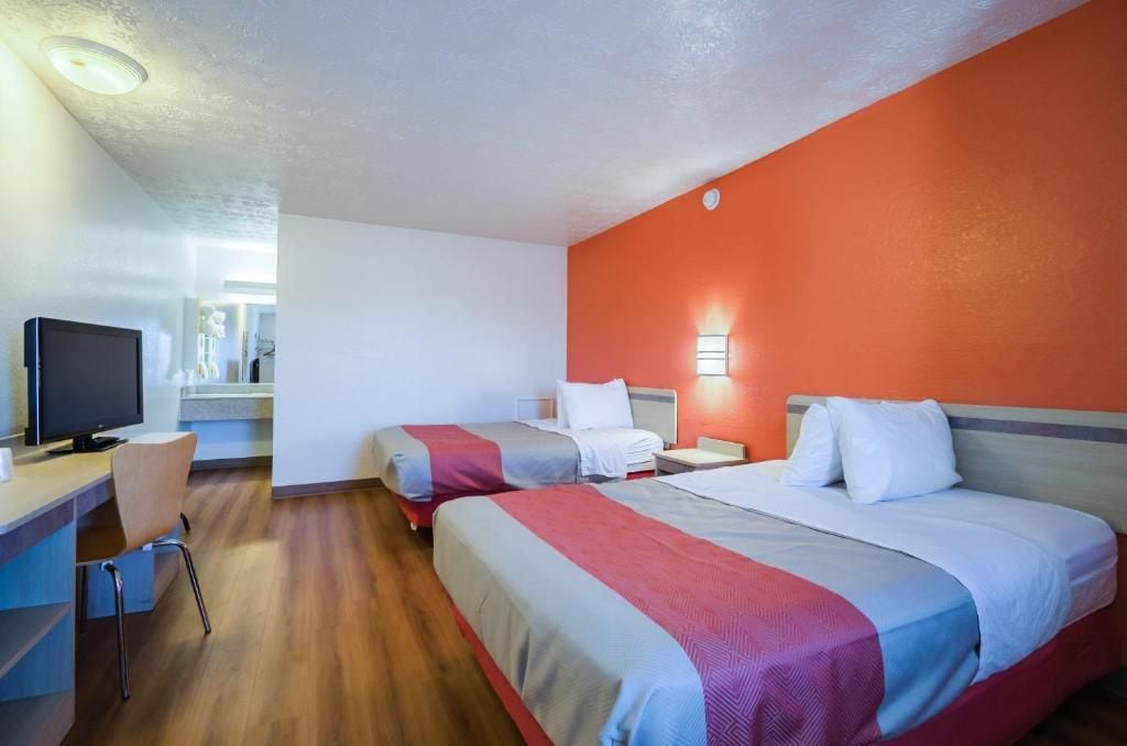 A hotel room with two beds, a desk with a chair, a television, and a window.