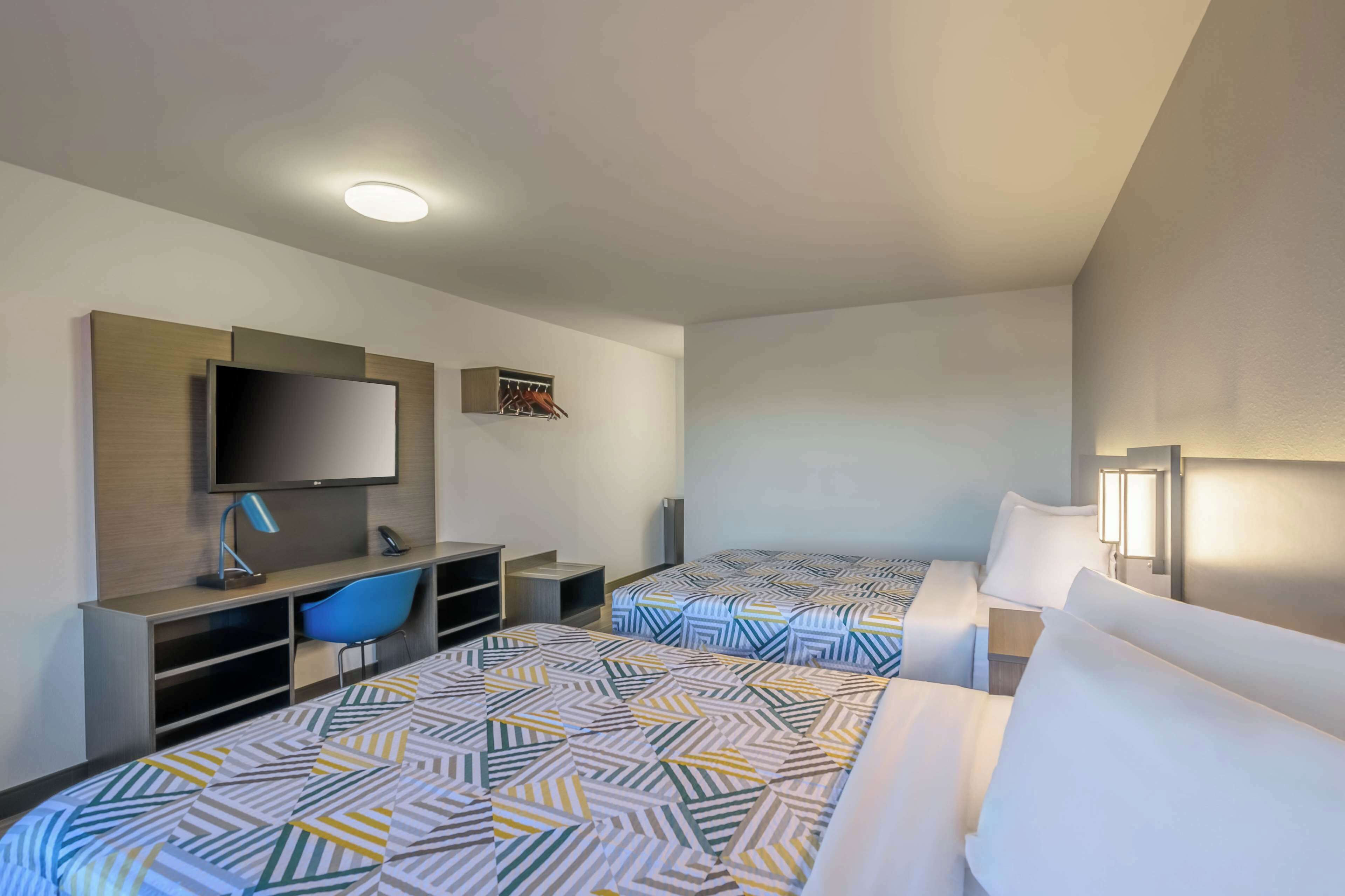 A hotel room with two beds, a desk with a chair, a flat-screen TV, and a small closet.
