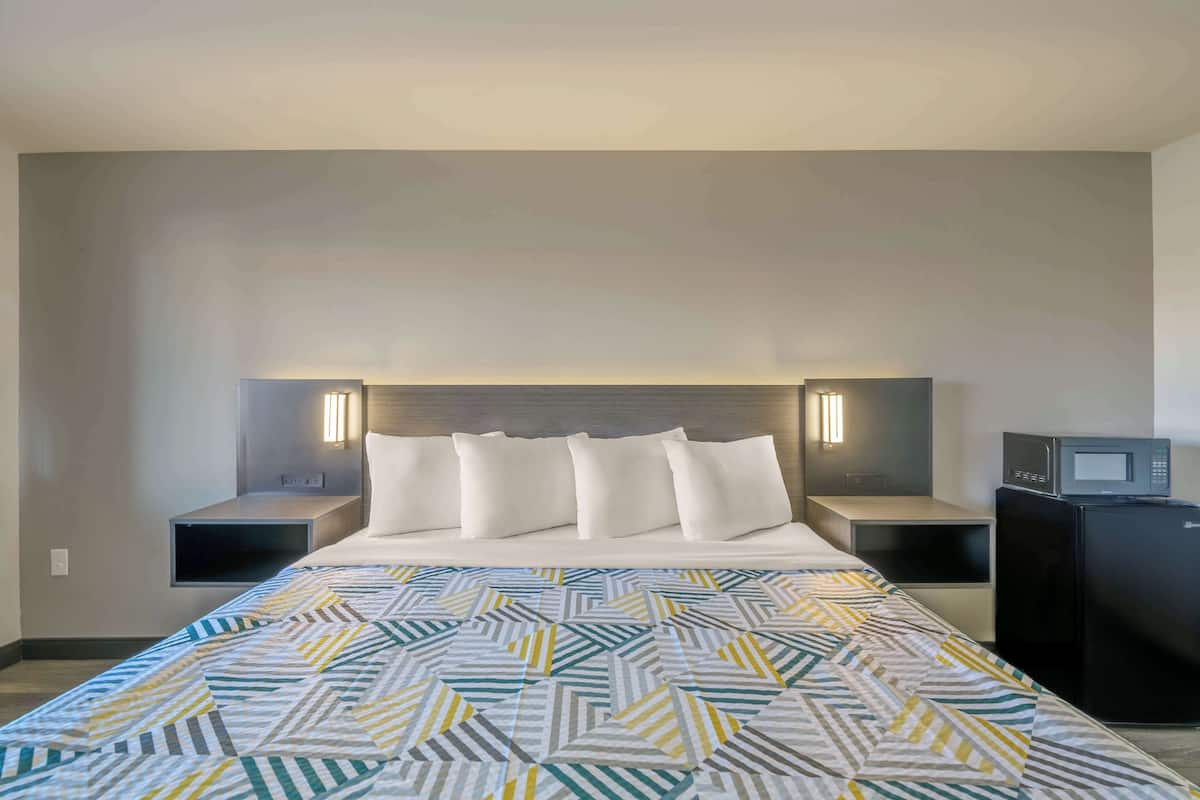 A hotel room with a bed, two bedside tables, a microwave, and a refrigerator.