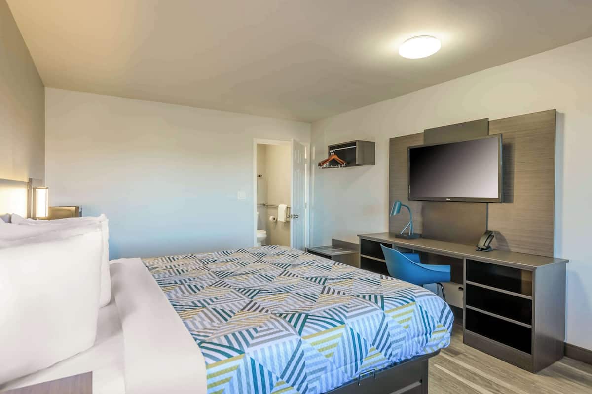 A hotel room with a bed, a desk, a chair, a TV, and a wardrobe.
