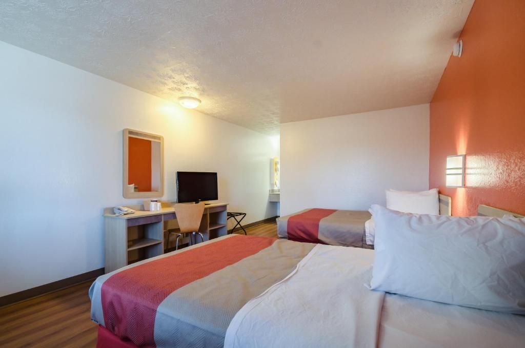 A hotel room with two beds, a desk, a chair, a television, and a mirror.
