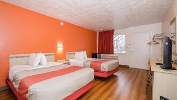 A hotel room with two beds, a desk with a computer, and a window with red curtains.