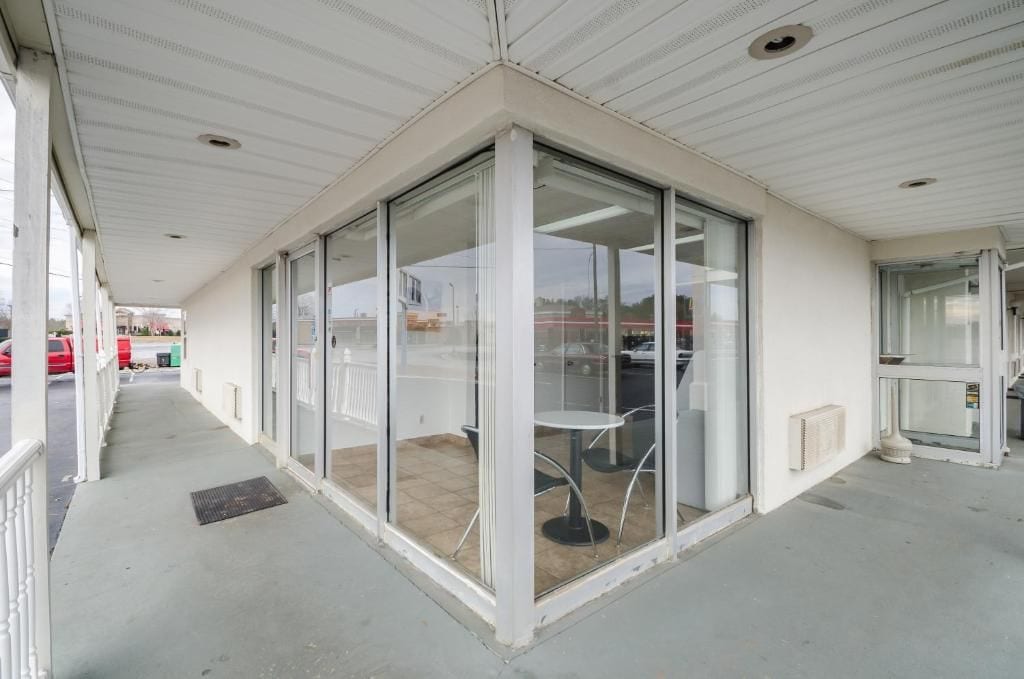 Un espacio exterior techado con puertas de vidrio que dan a un ambiente interior, una pequeña mesa con sillas y vista a la calle.