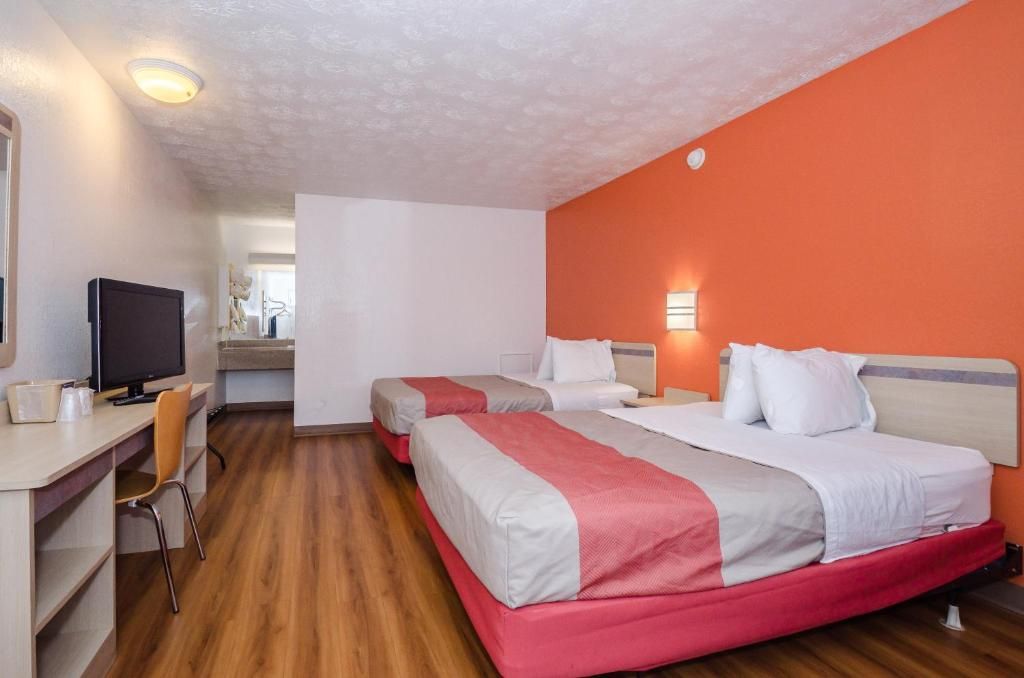 Una habitación de hotel con dos camas, un escritorio, una silla, un televisor y un baño a la vista.