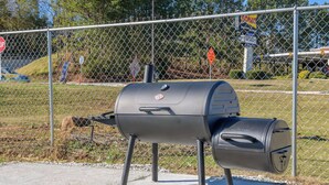 Ein tragbarer Grill mit Deckel und Seitenbrenner, auf einem Betonfundament platziert.