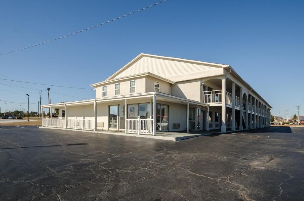 A two-story building with a balcony on the second floor, a covered front porch, and a parking lot in front.