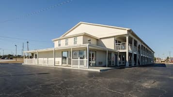 A two-story building with a balcony on the second floor, a covered front porch, and a parking lot in front.