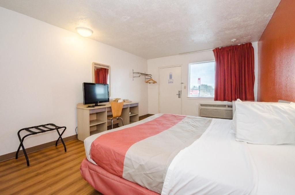 Habitación de hotel con cama, escritorio, televisor y ventana con cortinas.