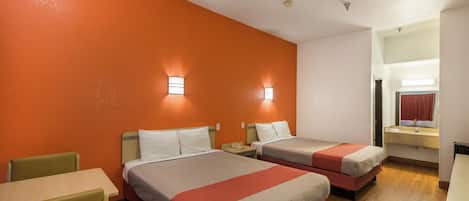 Camera d'albergo con due letti, un tavolino e bagno con specchio e lavandino.