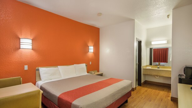 Une chambre d’hôtel comprenant un lit, un bureau, une chaise, ainsi qu’une salle de bain avec un miroir et un lavabo.