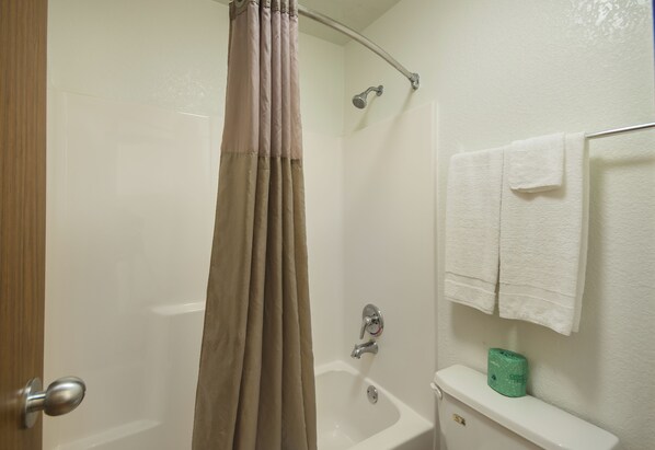 A bathroom with a shower curtain, a bathtub, a toilet, and a towel rack with towels.