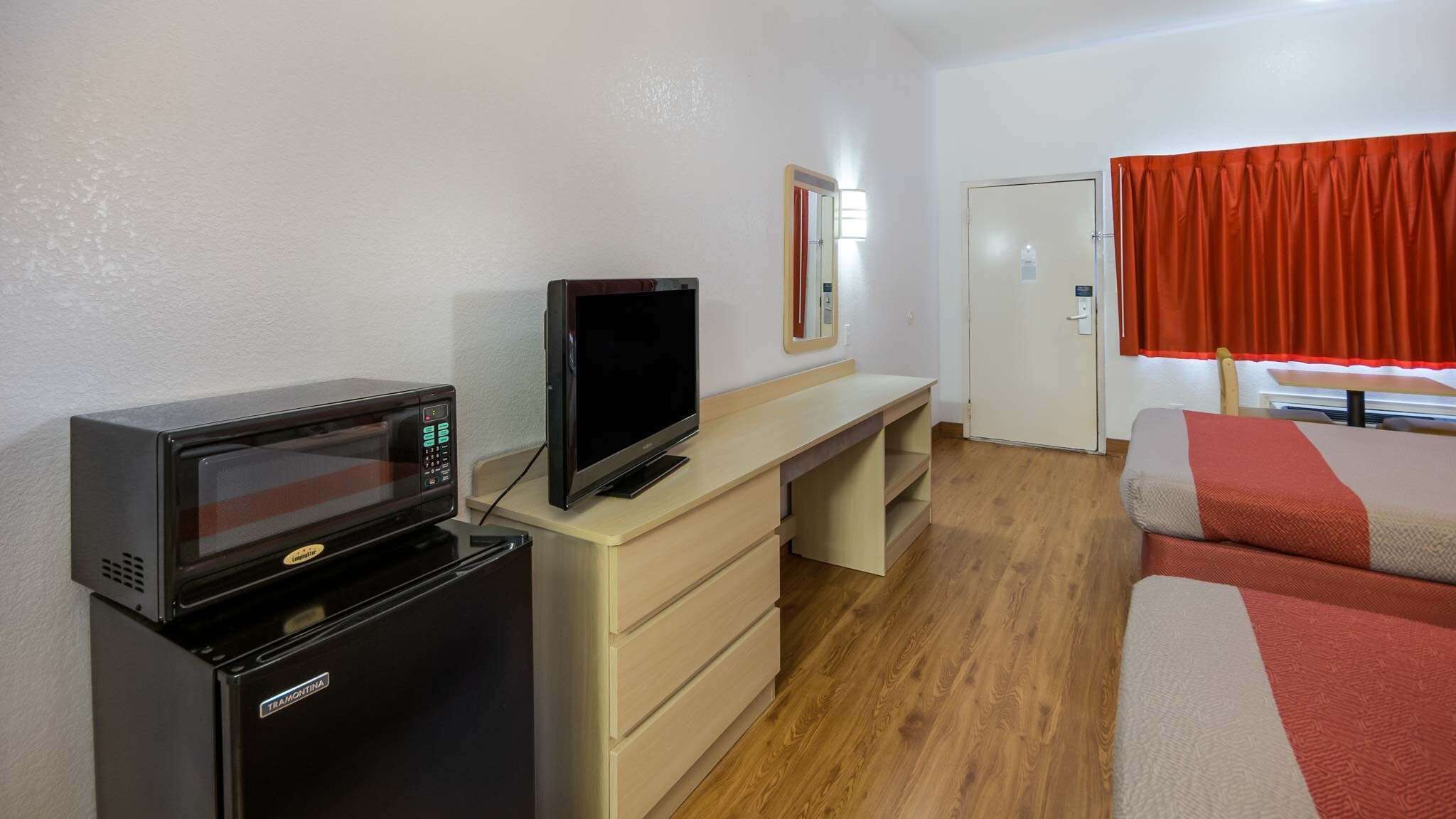 A compact room with a microwave, a television, a small refrigerator, a desk, a chair, and a bed.