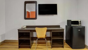 Una habitación con escritorio, silla, televisión de pantalla plana y refrigerador negro.