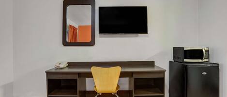 A room with a desk, a chair, a flat-screen TV, and a black refrigerator.