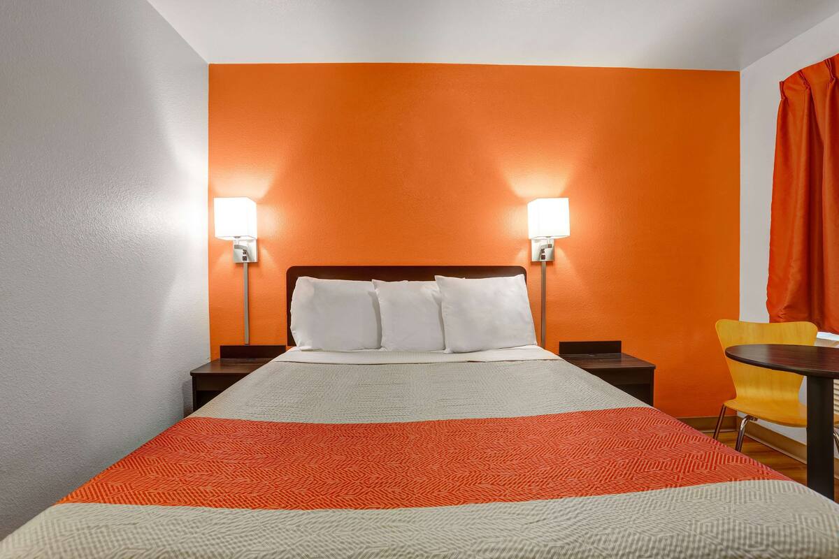 Una habitación de hotel con una cama, dos mesitas de noche, una silla y una pequeña mesa.