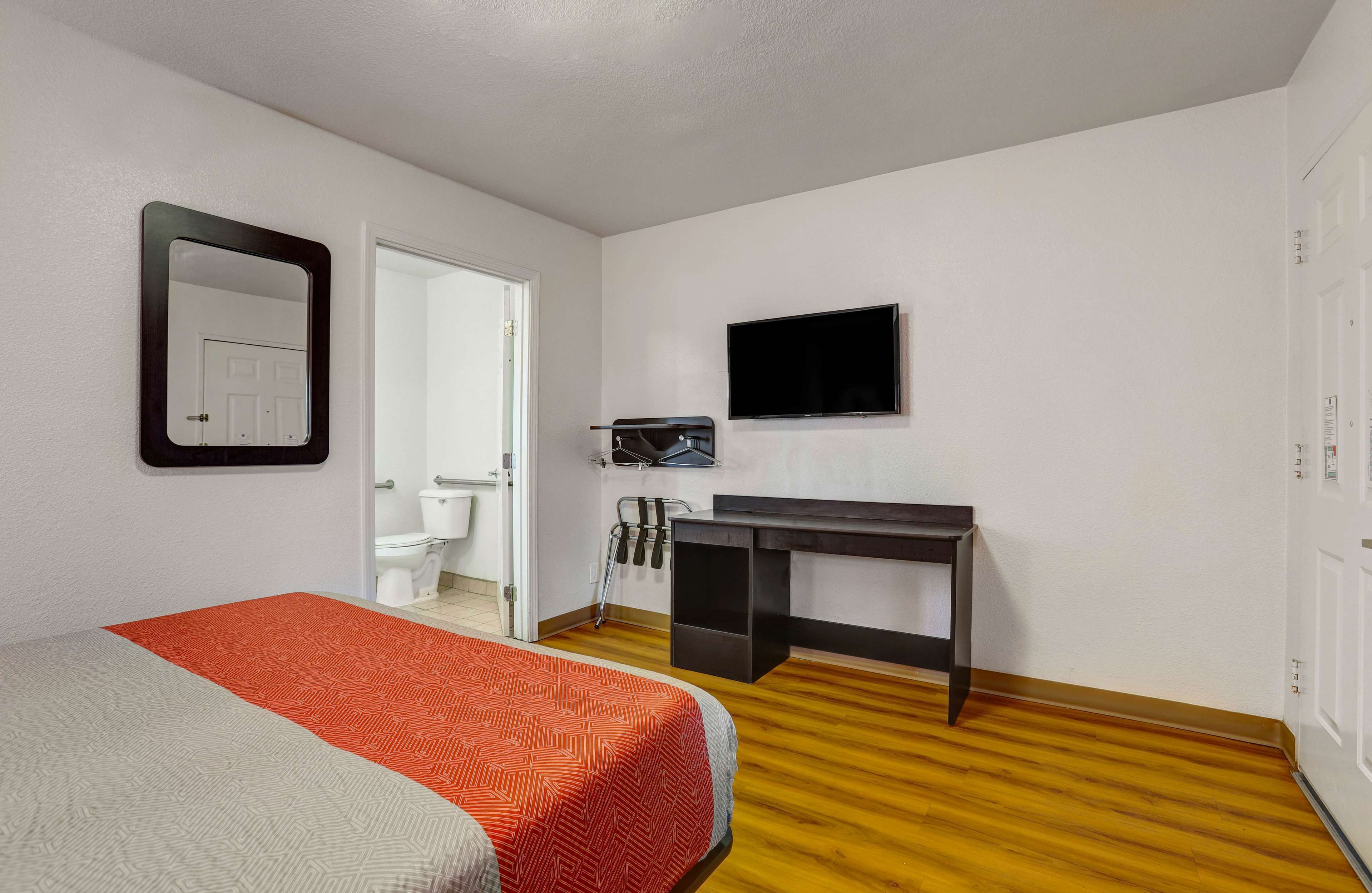 Un dormitorio con cama, escritorio, televisión y baño visible a través de una puerta abierta.