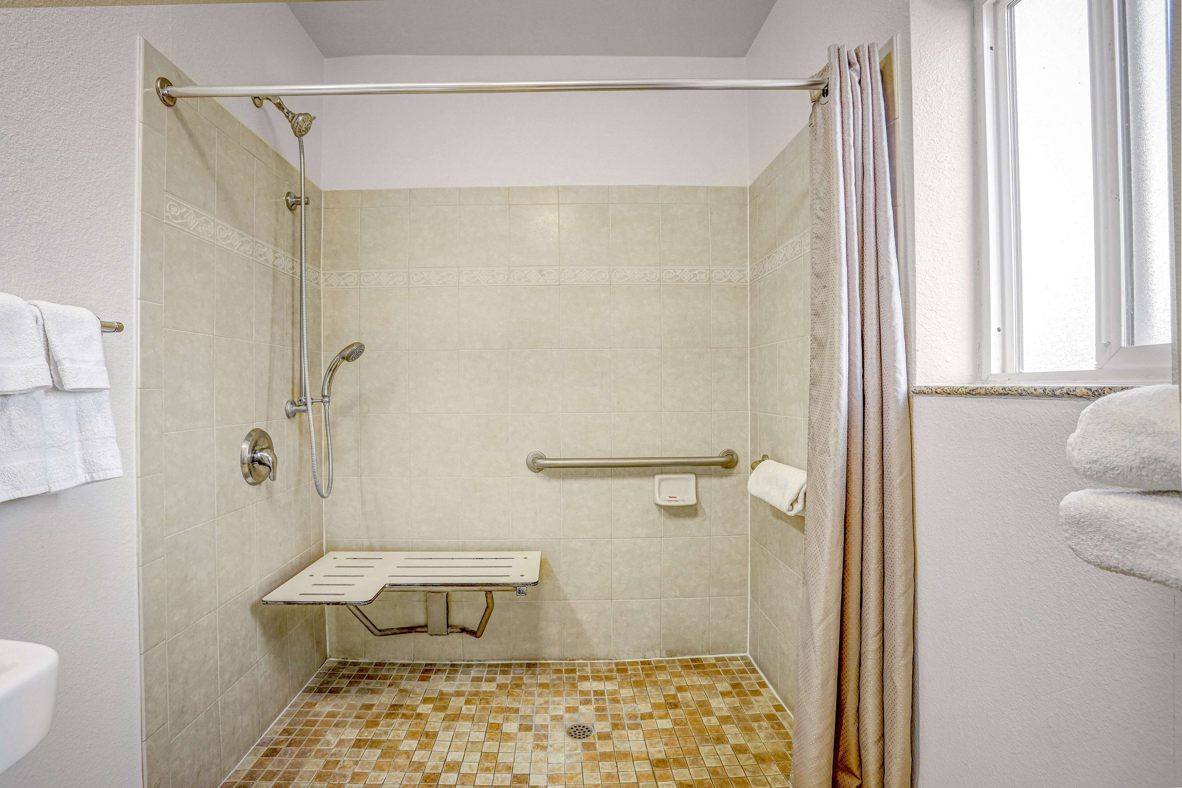 A shower with a grab bar, a bench, and a hand dryer.