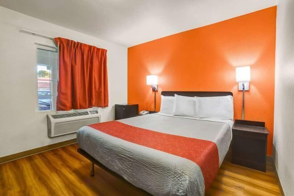 Una habitación de hotel con una cama, un calefactor, una ventana con cortinas y dos lámparas fijadas a la pared.