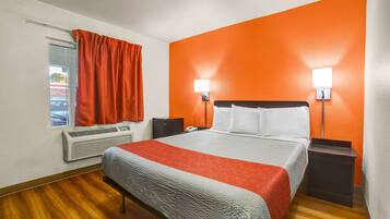 A hotel room with a bed, two bedside lamps, a heater, and a window with curtains.