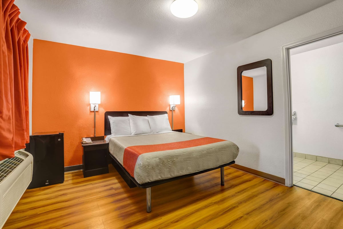 Habitación de hotel con una cama, dos lámparas de noche, una mesita de noche, un equipo de aire acondicionado y una puerta.