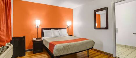 A hotel room with a bed, two bedside lamps, a nightstand, an air conditioning unit, and a door.