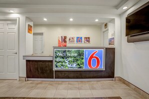 A reception desk with a large sign, a wall-mounted TV, and framed pictures. - Motel 6 Marysville, CA (Marysville)