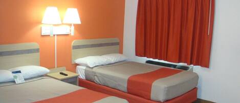 A hotel room with two beds, a nightstand, a lamp, and a window with curtains.