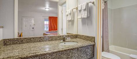 A bathroom with a granite countertop sink, a white toilet, and a shower area.