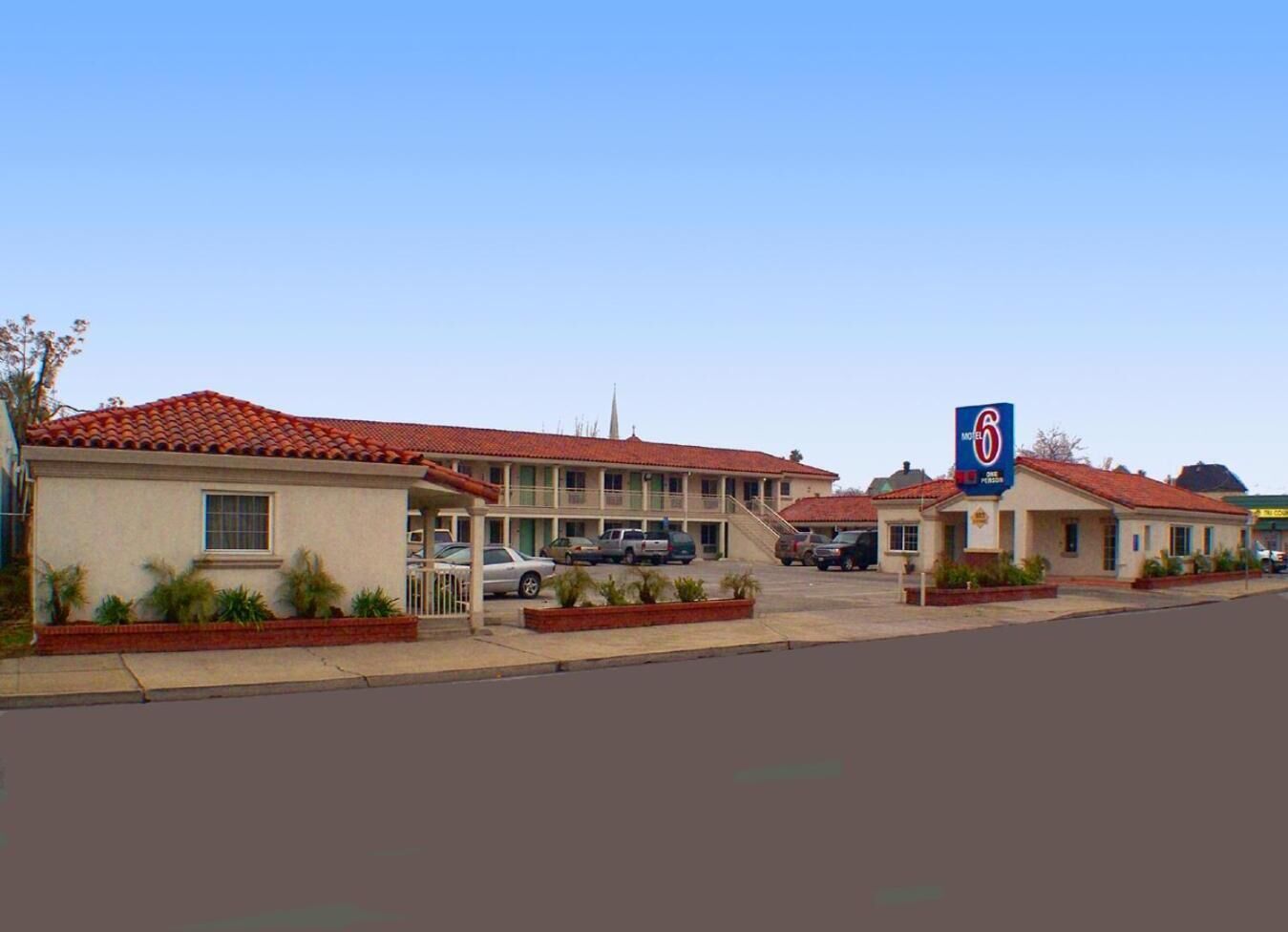 Um motel com telhado de telhas vermelhas, estacionamento e uma placa indicando que é um Motel 6.