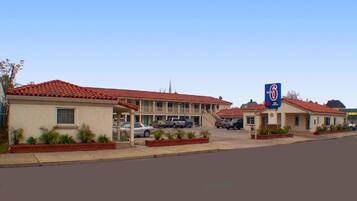 Um motel com telhado de telhas vermelhas, estacionamento e uma placa indicando que é um Motel 6.