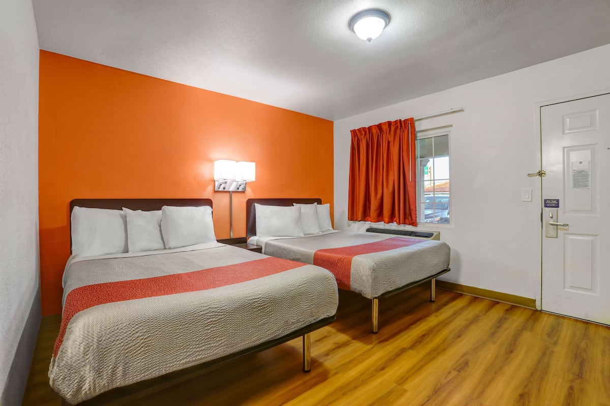 Habitación de hotel con dos camas, una ventana con cortinas naranjas, una puerta blanca y una lámpara en el techo.