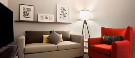 A living room with a sofa, a red armchair, a floor lamp, and framed artwork on the wall.