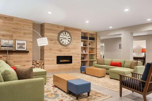 A modern living room with a fireplace, green sofas, a wooden coffee table, and a clock on the wall. - Country Inn & Suites by Radisson, Shreveport-Airport, LA (Shreveport)