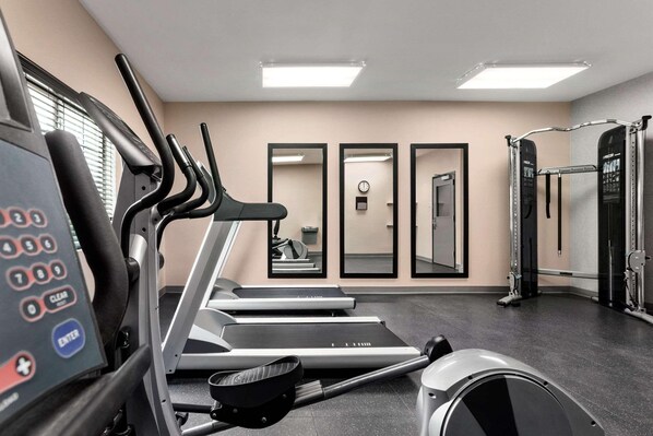 A gym with treadmills, a control panel, mirrors, and a weightlifting area.