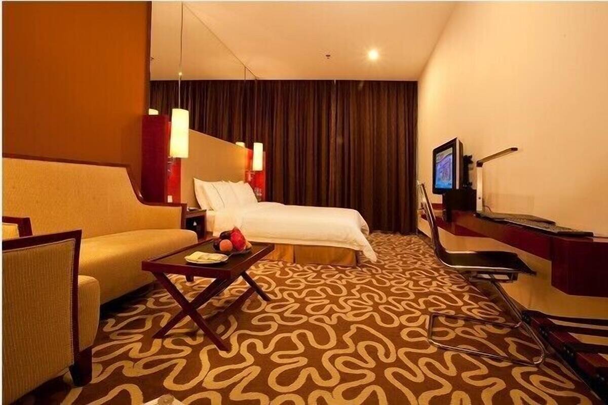 A hotel room with a bed, a sofa, a small table with fruits, a TV, and a desk with a computer.