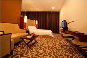 A hotel room with a bed, a sofa, a small table with fruits, a TV, and a desk with a computer. - CAA Holy Sun Hotel (Shenzhen)