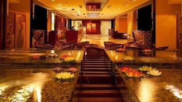 A hotel lobby with a central staircase, seating area, and a reception desk.