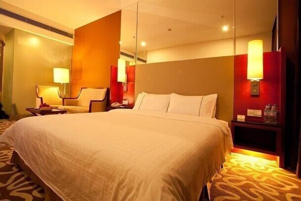 A hotel room with a large bed, a chair, a nightstand, and a wall-mounted lamp.