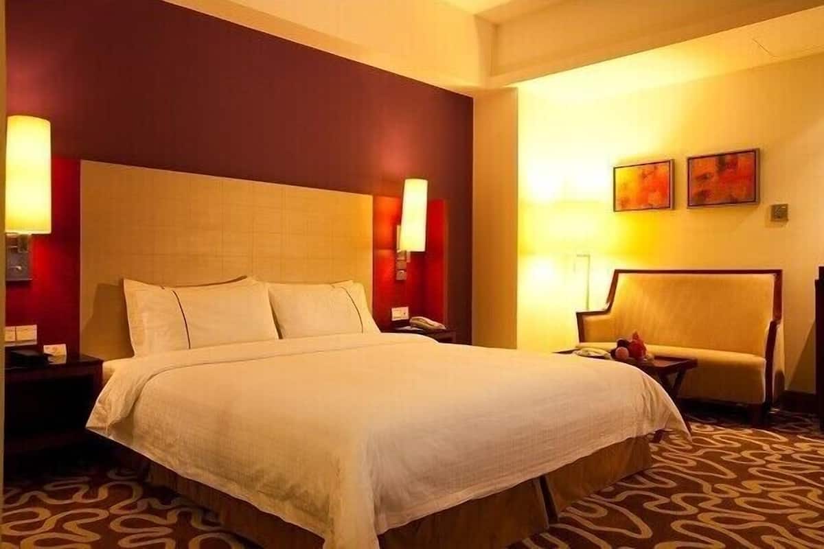 A hotel room with a large bed, two bedside tables, a chair, and two wall-mounted lamps.