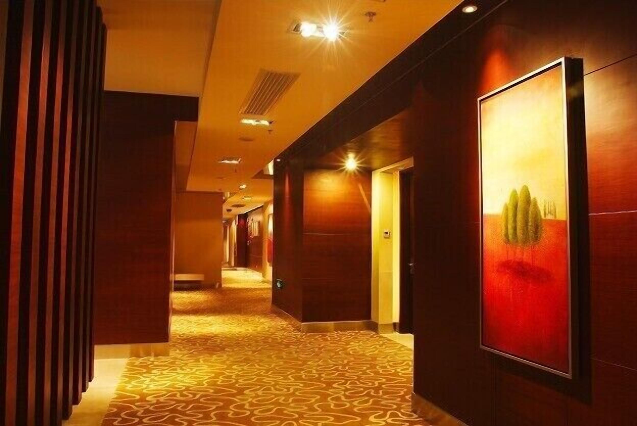 A hotel corridor with patterned carpet, wooden walls, and framed artwork.