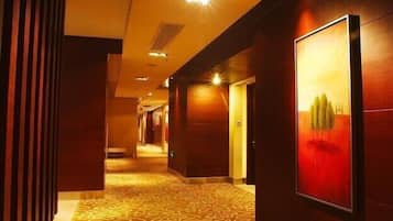 A hotel corridor with patterned carpet, wooden walls, and framed artwork.