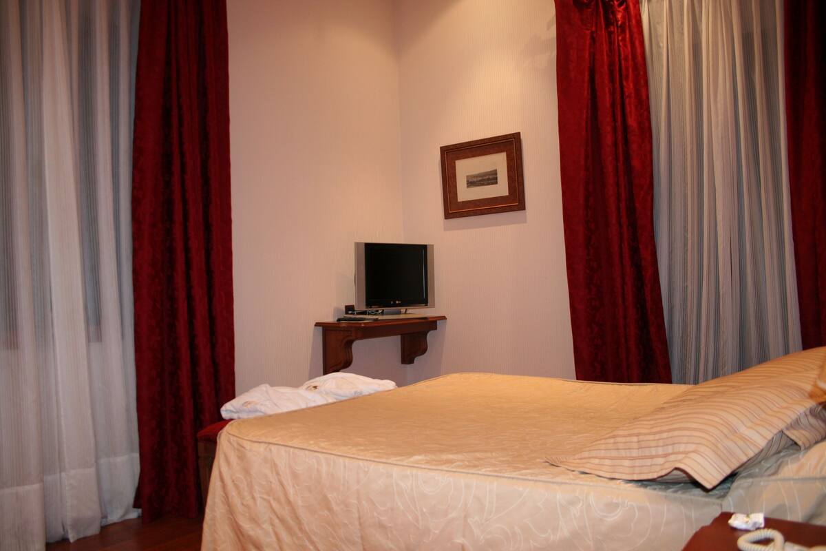 A hotel room with a bed, a television on a wooden stand, and a framed picture on the wall.