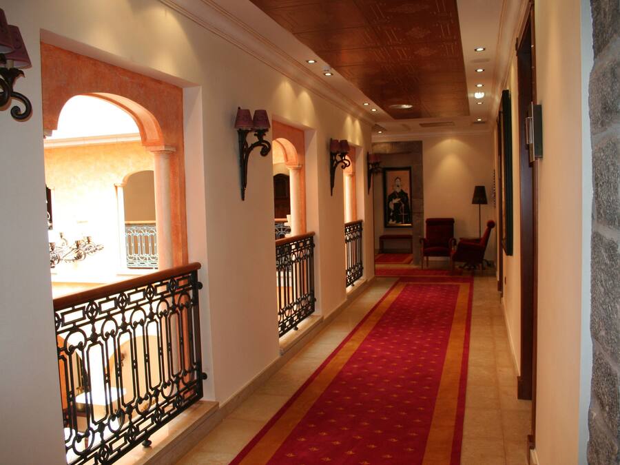 A corridor with a red carpet, ornate black railings, and a stone wall on the right.