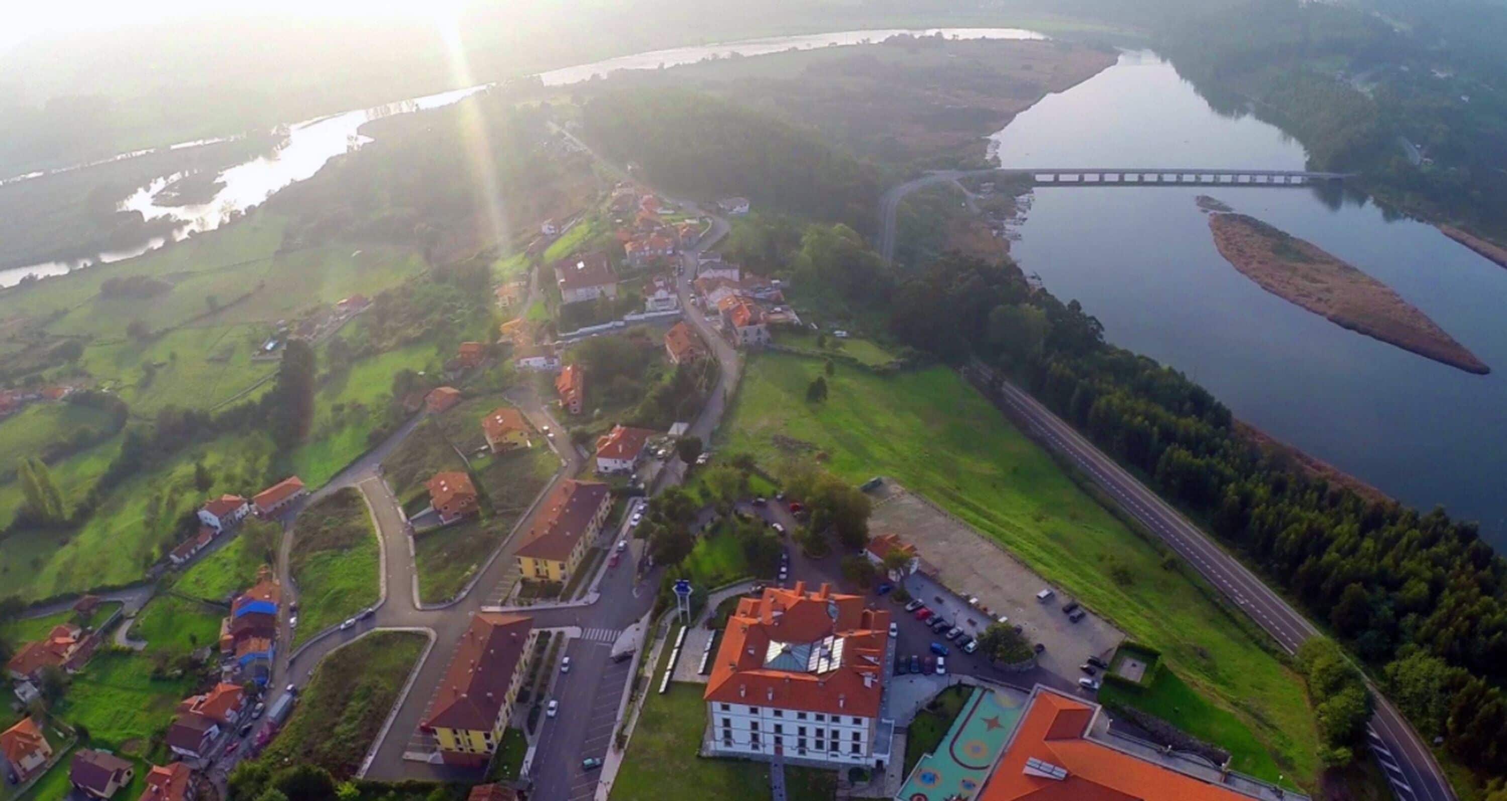 An aerial view of a small town with a river, a bridge, and a mix of residential and commercial buildings.