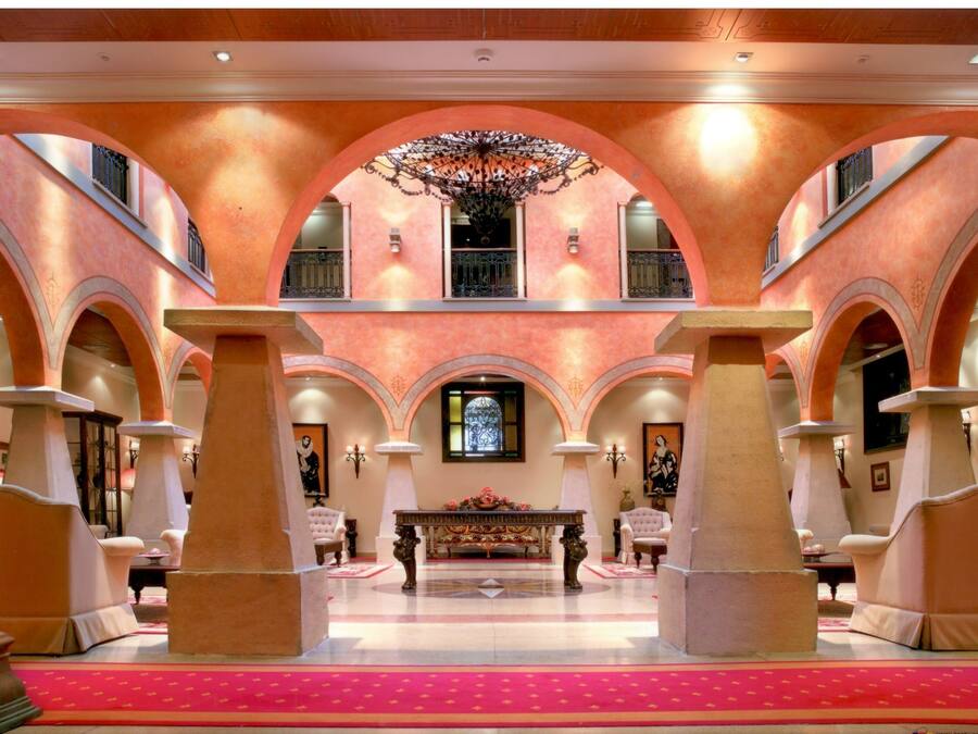 Un salón amplio con techo alto, columnas abovedadas y un candelabro central.