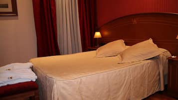 Una cama bien hecha con un cabecero, una mesita de noche con lámpara y una cortina roja.